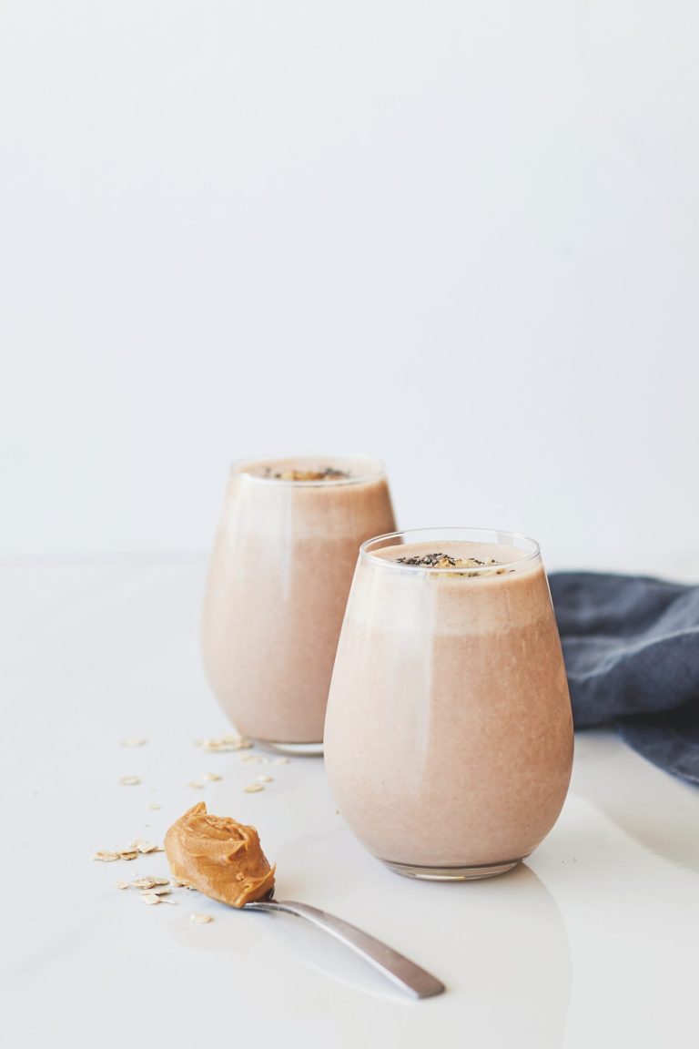 Nutty Goodness: Healthy Protein Peanut Butter Smoothie 4 Two glasses of peanut butter banana oat smoothie with chia, spoonful of peanut butter on white counter