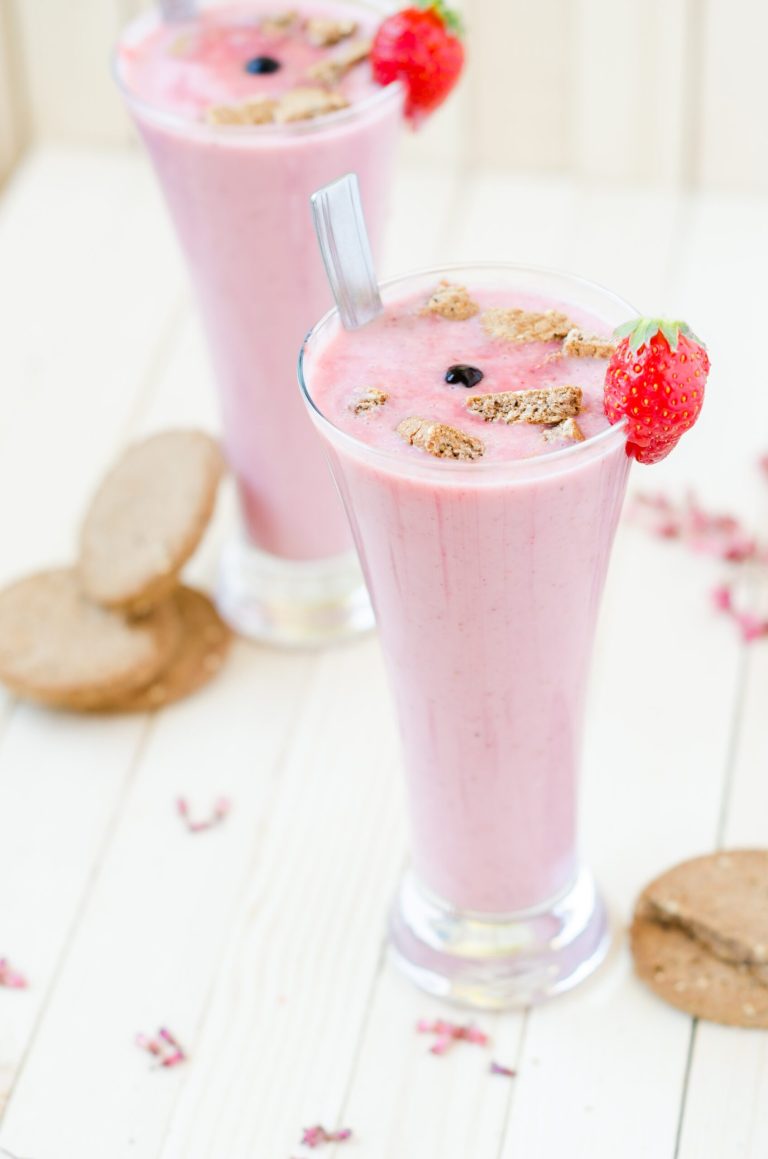 Strawberry Ginger Snap Smoothie: A Fusion of Flavors 3 Tall glasses of strawberry smoothie with granola crumble and fresh berries on a light wooden table